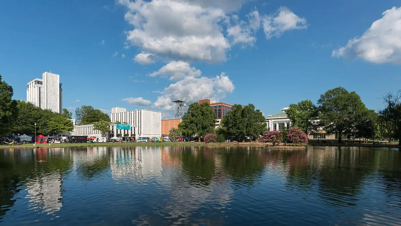 Pond with downtown office buildings and trees reflected in the water under a blue sky