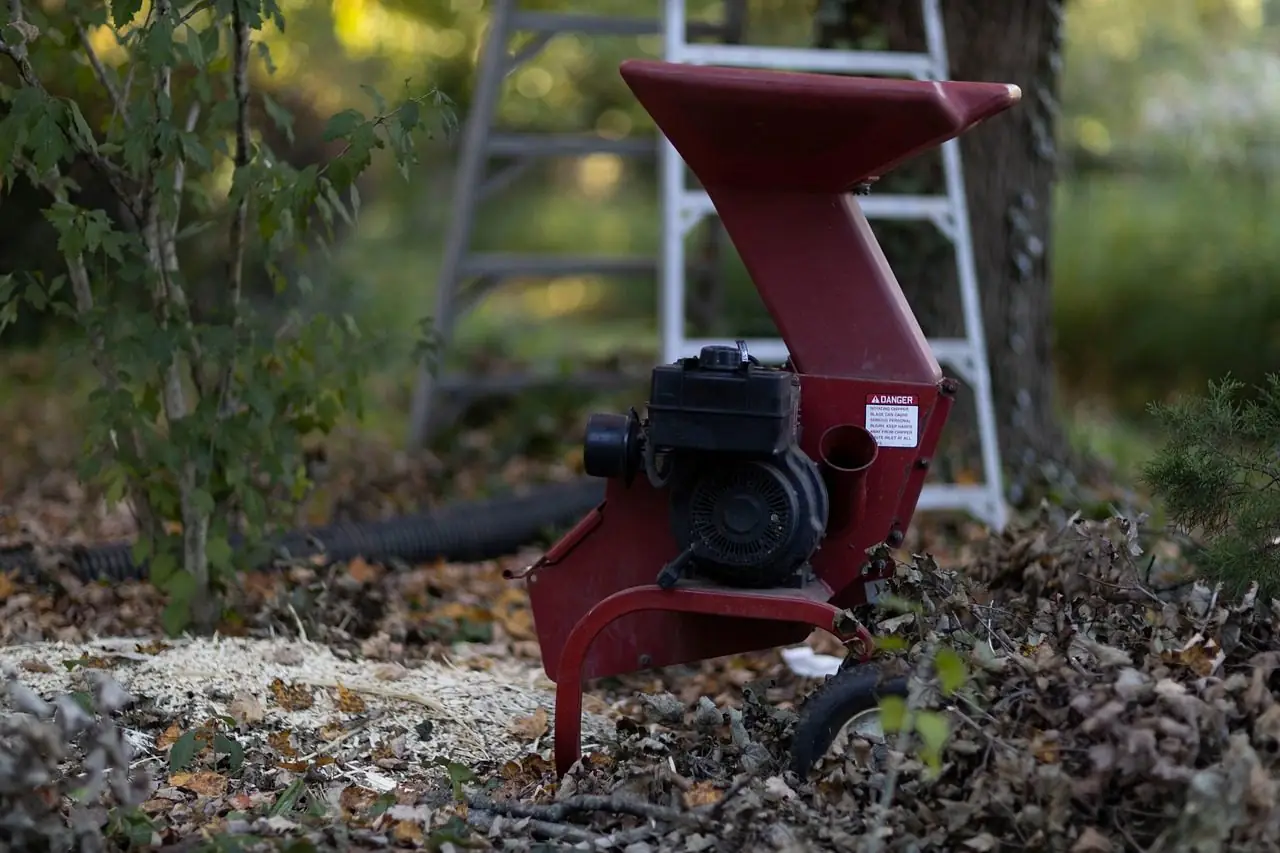 Small red wood chipper on leafy ground beside a wooded yard