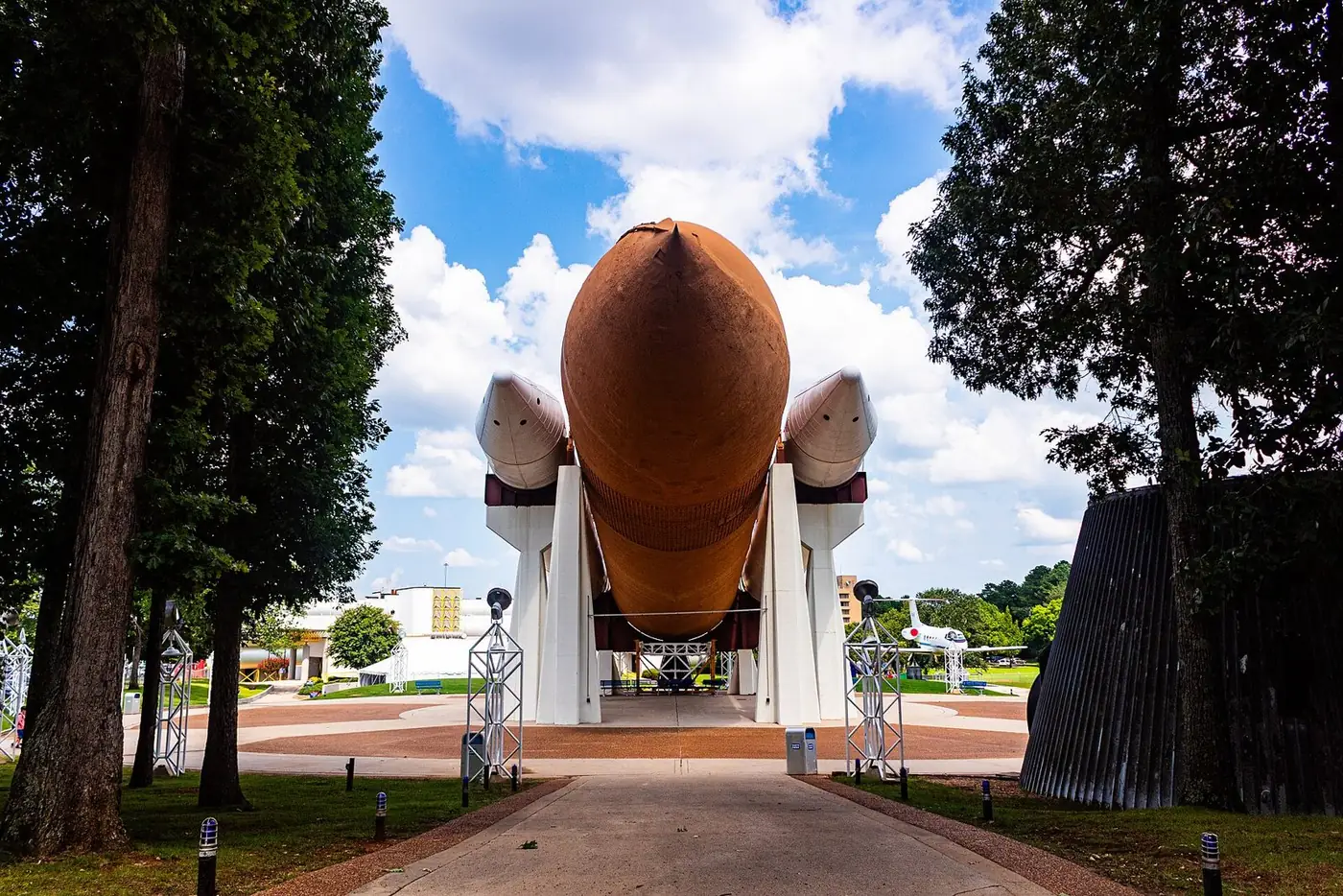 Large orange external tank and white boosters of a space shuttle display framed by tall trees